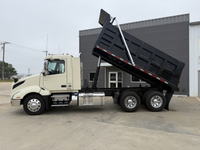 Volvo VNL300 dump truck with bed raised showing side profile and cab. Text on truck includes no visible labels; overall image depicts a beige cab with chrome fuel tanks and a black dump body in raised position.