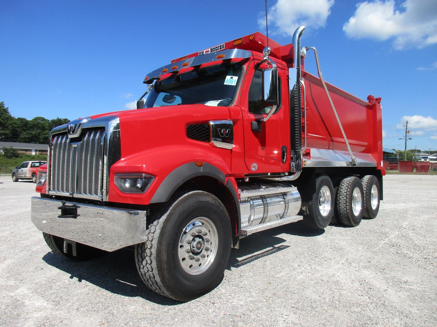 Western Star 49X dump truck in red with chrome grille and dual rear axles, side exhaust, and large dump bed visible.