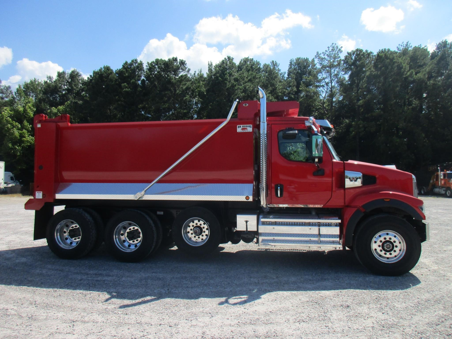 Western Star 49X dump truck side view showing red dump body and chrome fuel tanks.