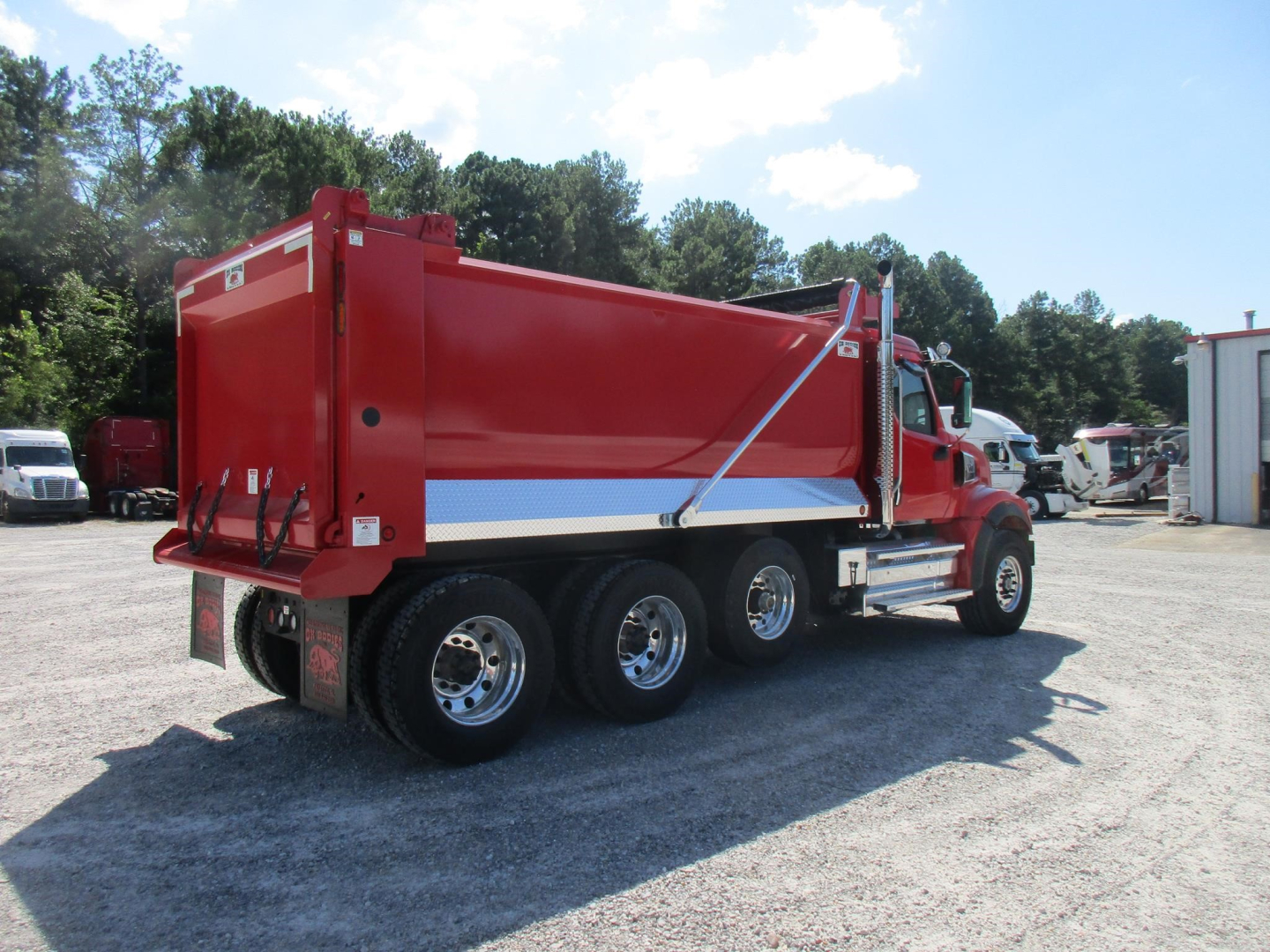 Dump truck side view showing red Western Star 49X dump bed with chrome dual rear axles and blue/white reflective stripe.
