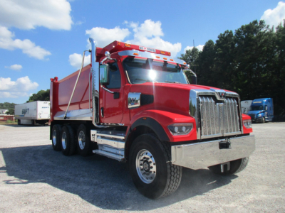 Red Western Star 49X dump truck in a parking lot, side view, with chrome grille, dual rear axles, and a dump bed.