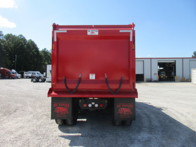 Rear view of red dump truck bed on a Western Star 49X, showing the tailgate with black lifting chains and mud flaps, dealership lot in background.