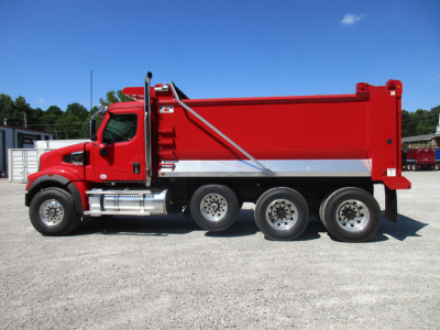 Western Star 49X dump truck side view showing red dump body, chrome fuel tanks, and triple rear axles in a gravel lot.
