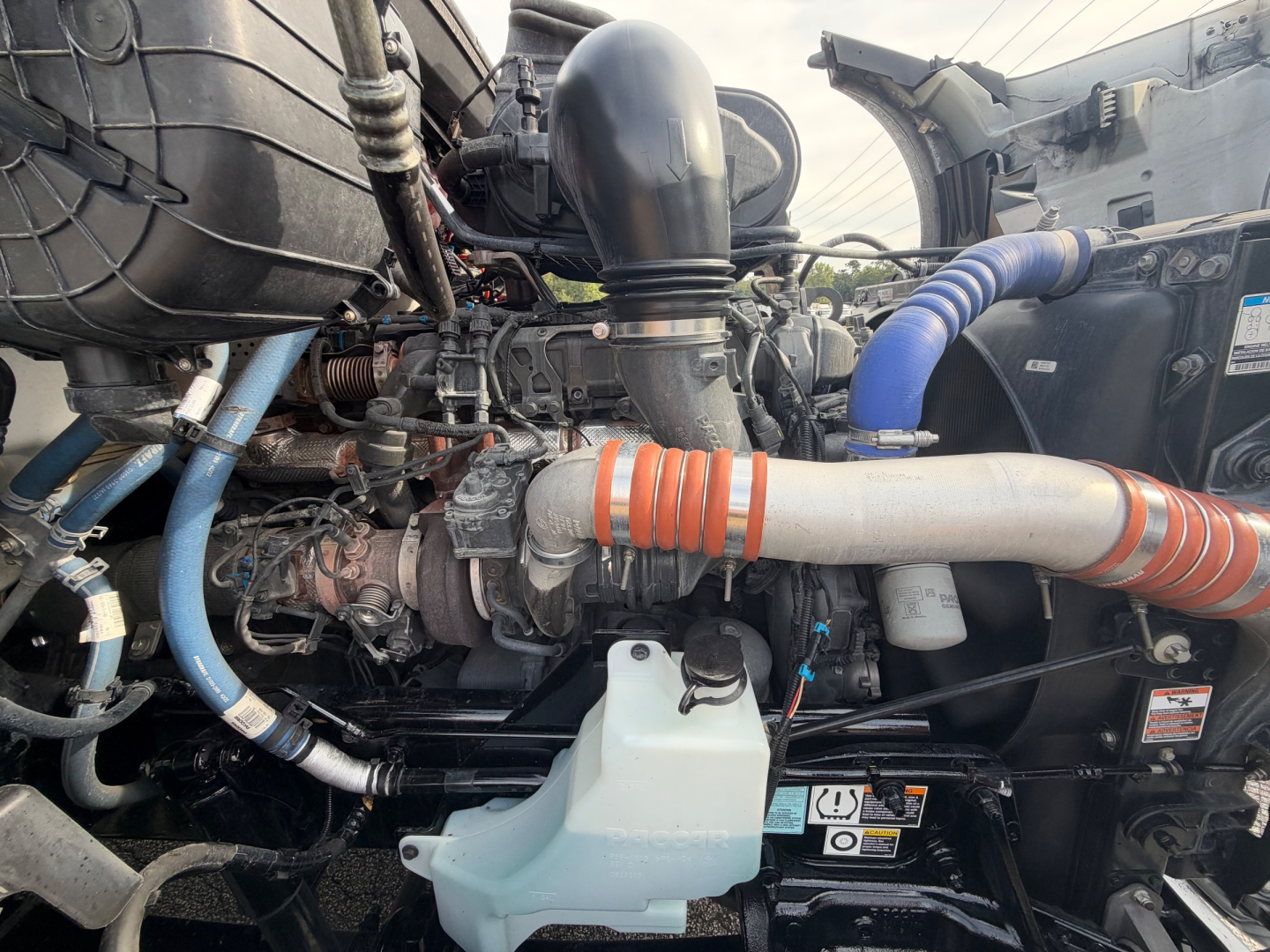 Kenworth T680 engine bay showing intake tubing, coolant reservoir, and various hoses