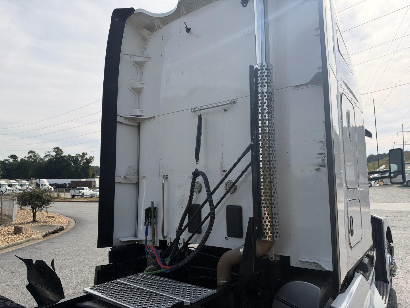 Kenworth T680 sleeper tractor rear view showing exhaust stack and wiring harnesses with white body, side panel, and bumper area visible.