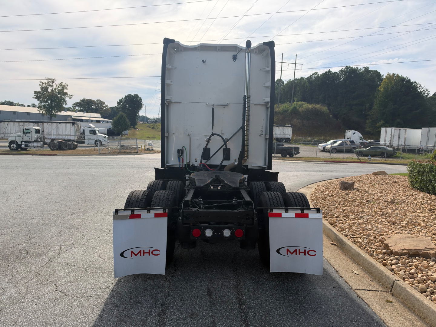 Kenworth T680 rear view showing fifth wheel area, dual rear axles, mud flaps labeled MHC, and white sleeper cab back with VIN/details grid visible.
