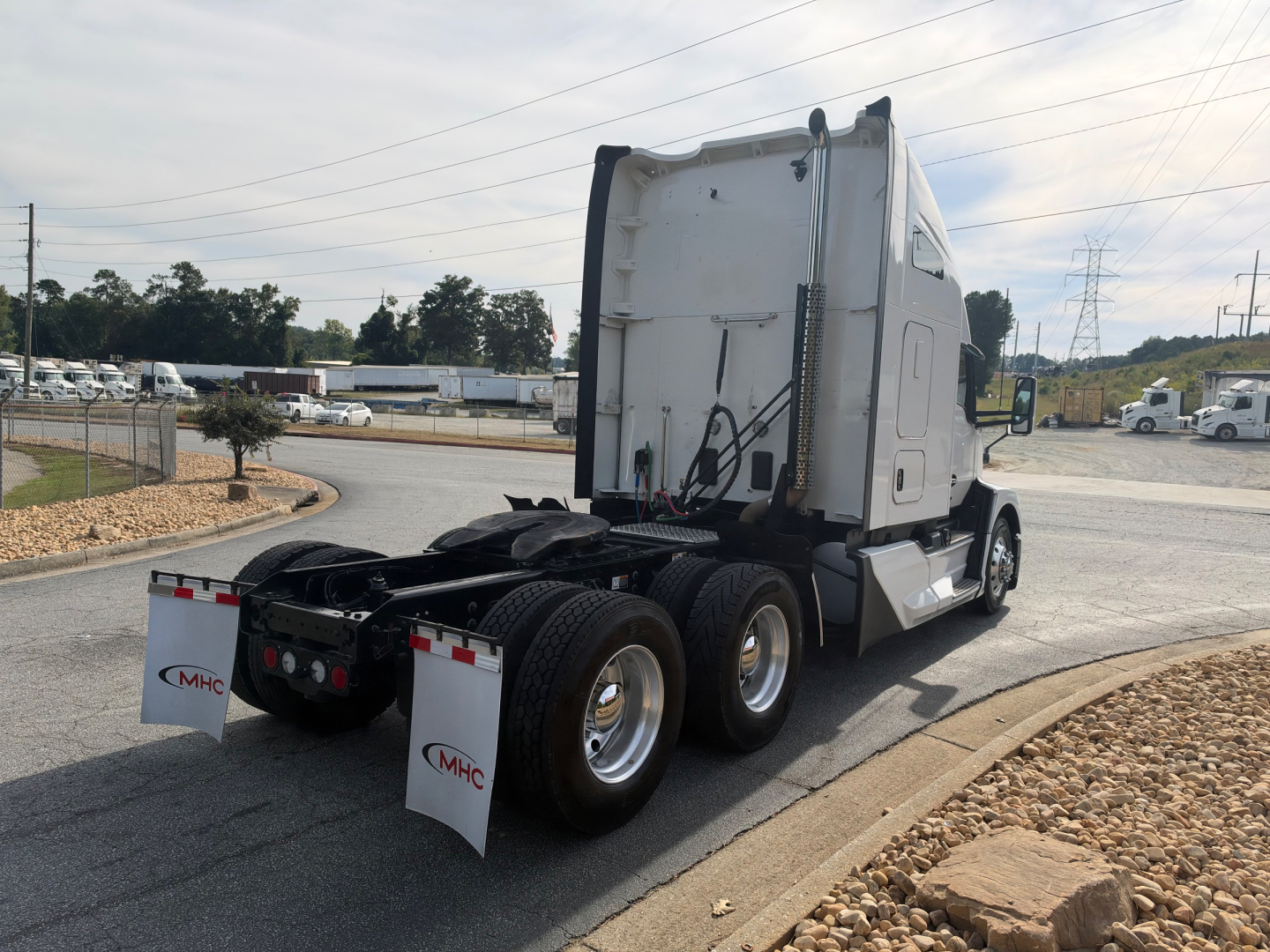 Kenworth T680 tractor rear and sleeper cab, triple rear axles, white mud flaps with MHC logo, chassis and wheels visible.