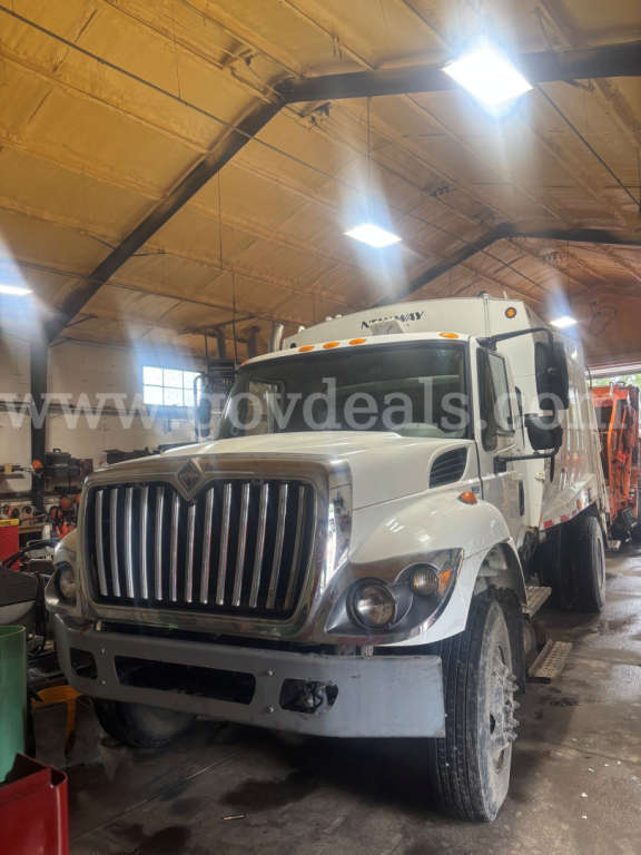 International 7400 dump truck in a garage showing front grille and side cab; heavy vehicle with white body and chrome grille.