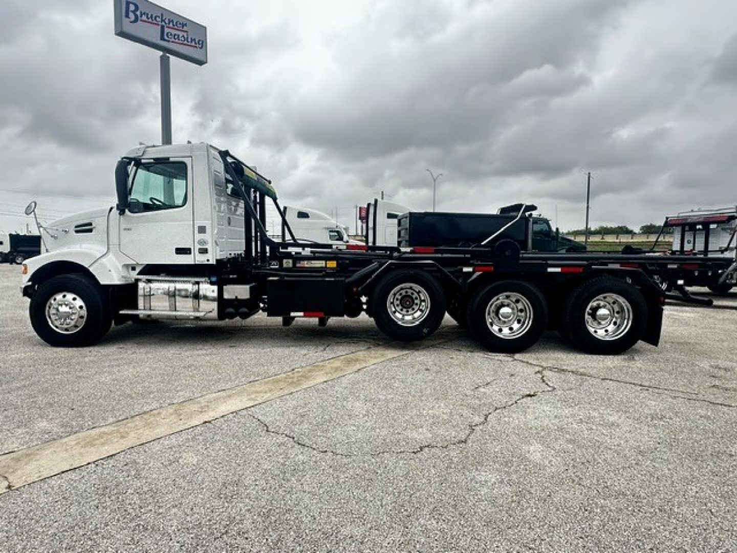 Volvo VHD 2020 roll-off truck side view showing white cab, heavy-duty flatbed trailer, rear dual-axle configuration, and VIN/stock details not visible on image.