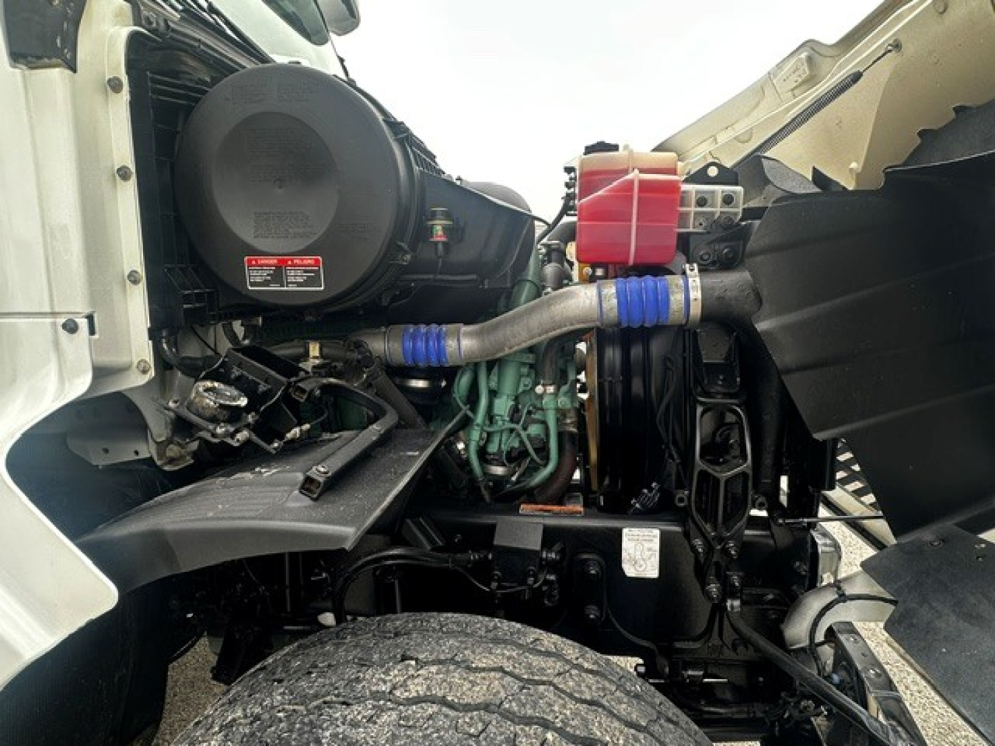 Volvo VHD engine bay showing air intake, coolant reservoir, hoses, and engine block with visible wiring and frame components.