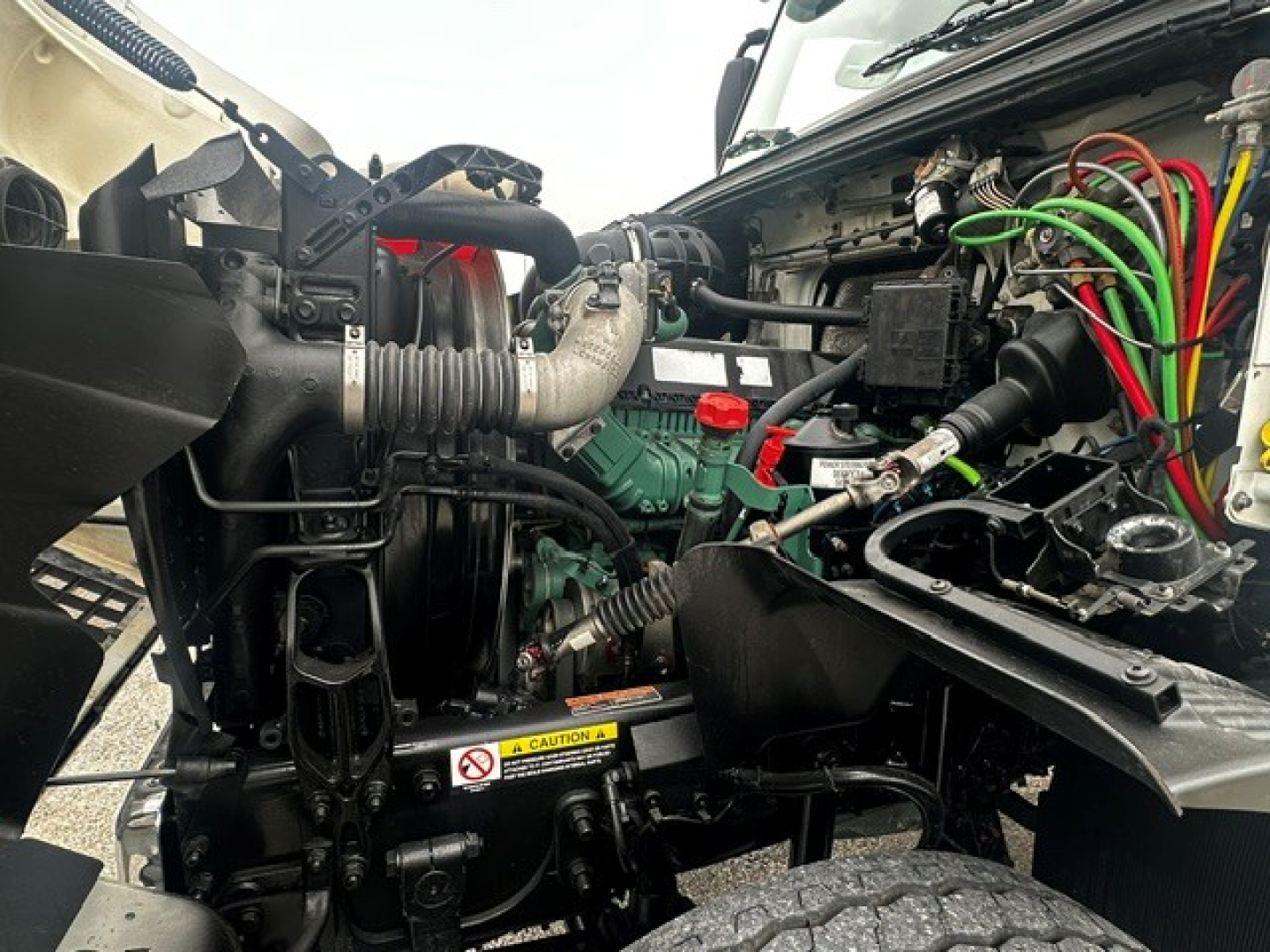 Volvo VHD engine bay view showing diesel engine, multiple hoses, green engine block, red and green electrical wires, and label stickers.
