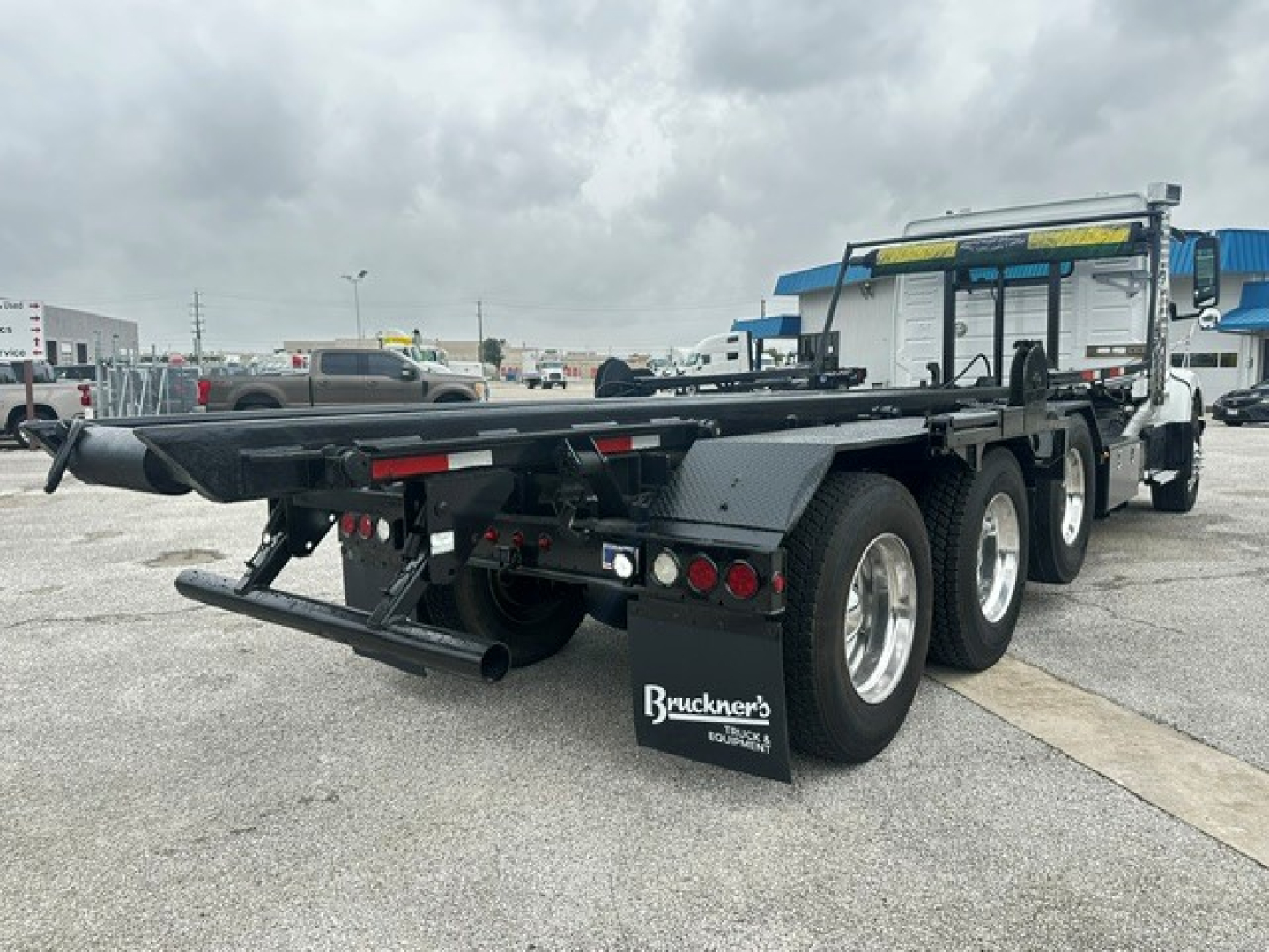 Rear view of a 2020 Volvo VHD rolloff truck showing triple axle and flatbed with mud flaps and taillights.