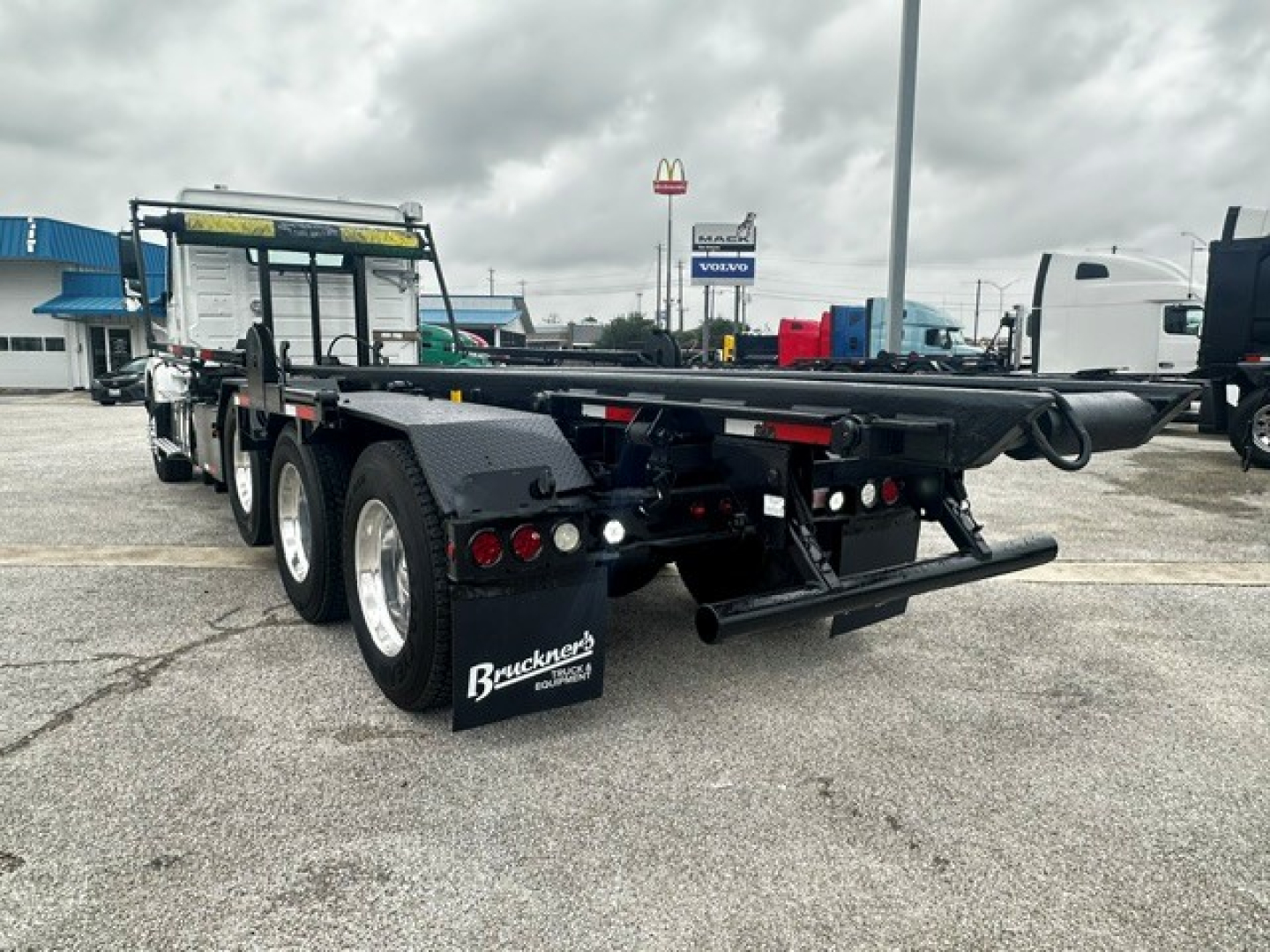 Rear and side view of a 2020 Volvo VHD rolloff truck showing dual rear axles, flatbed, rear bumper with taillights, mud flaps with Buckner tag, and equipment hitch.