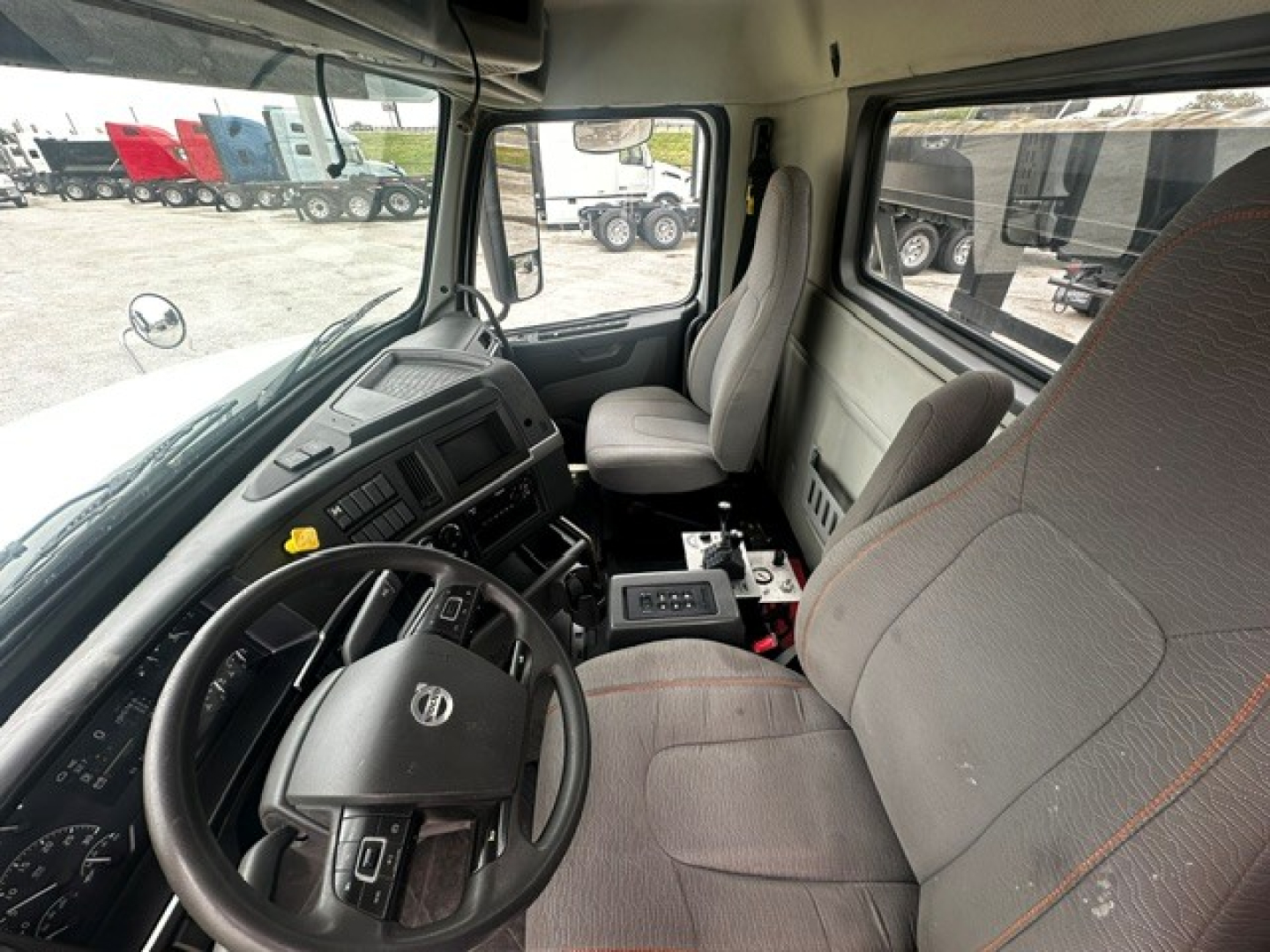 Interior of a Volvo VHD cab showing steering wheel, dashboard, and two seats with gray upholstery.
