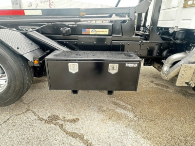 Truck frame side view showing a black toolbox with two latching handles, mounted under the chassis near the rear wheel on a 2020 Volvo VHD roll-off truck.
