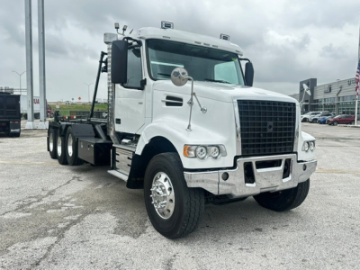 Truck cab and chassis of a white 2020 Volvo VHD rolloff truck, front three-quarter view, with large grille, dual mirrors, and dual rear axles.