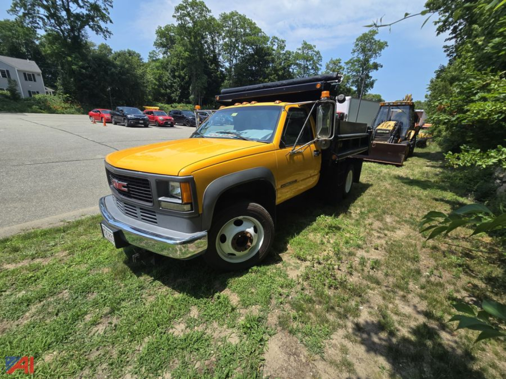 GMC Sierra Classic 3500 dump truck in yellow, front-left view, with dump bed and equipment on a grassy roadside.