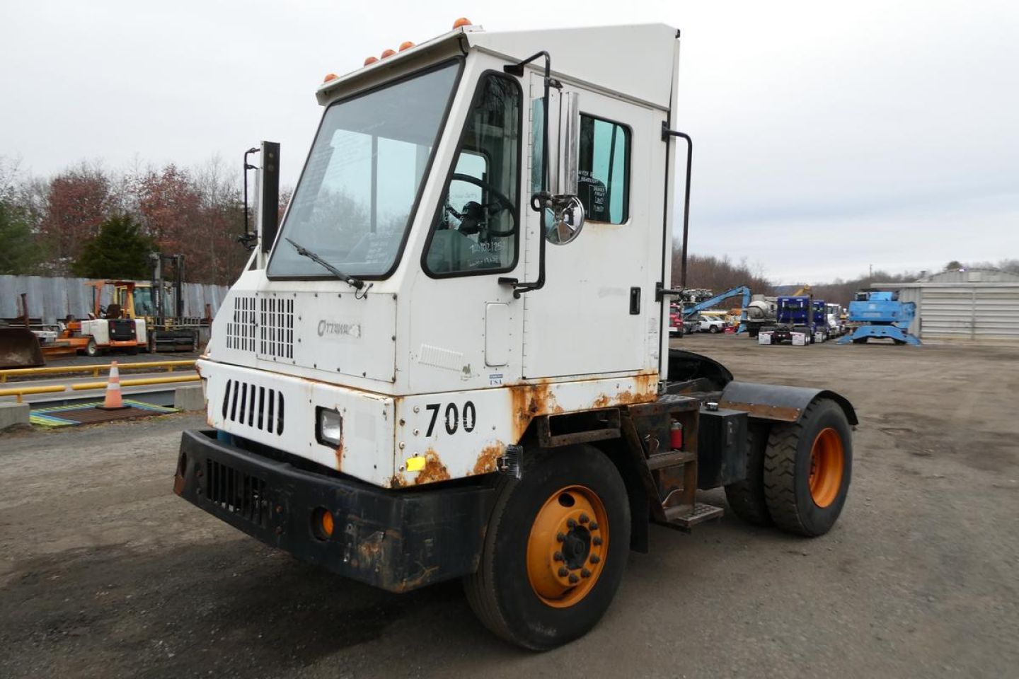 Truck cab showing white Ottawa yard truck with 700 and rusted lower front, front grille, and orange wheels in a storage yard.