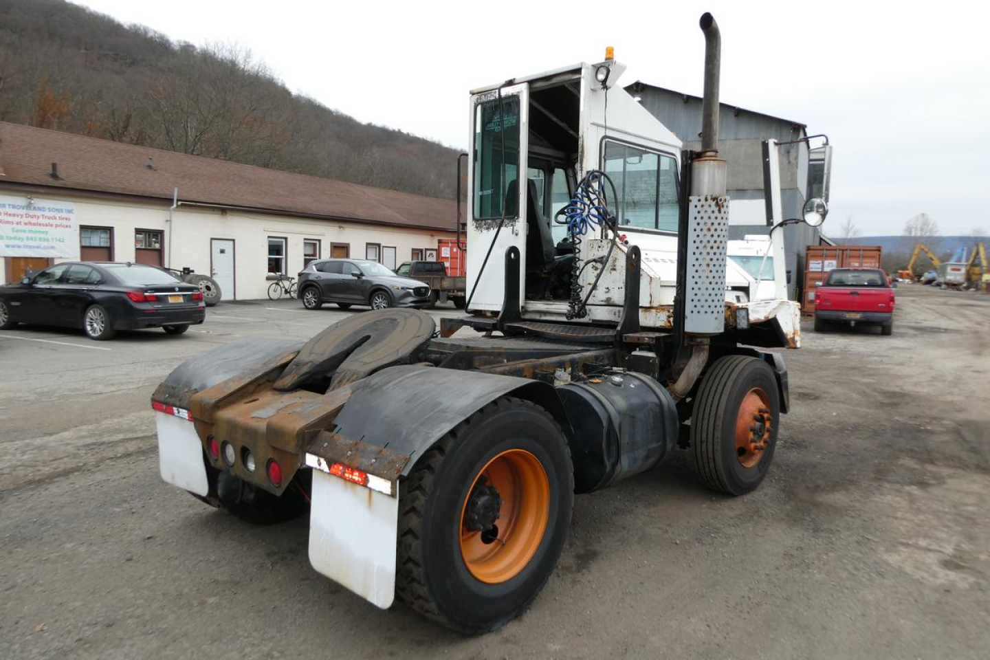 Truck chassis and cab of a used 2006 Ottawa yard truck showing rear view with dual rear axles, orange rims, fuel tanks, and exhaust stack.