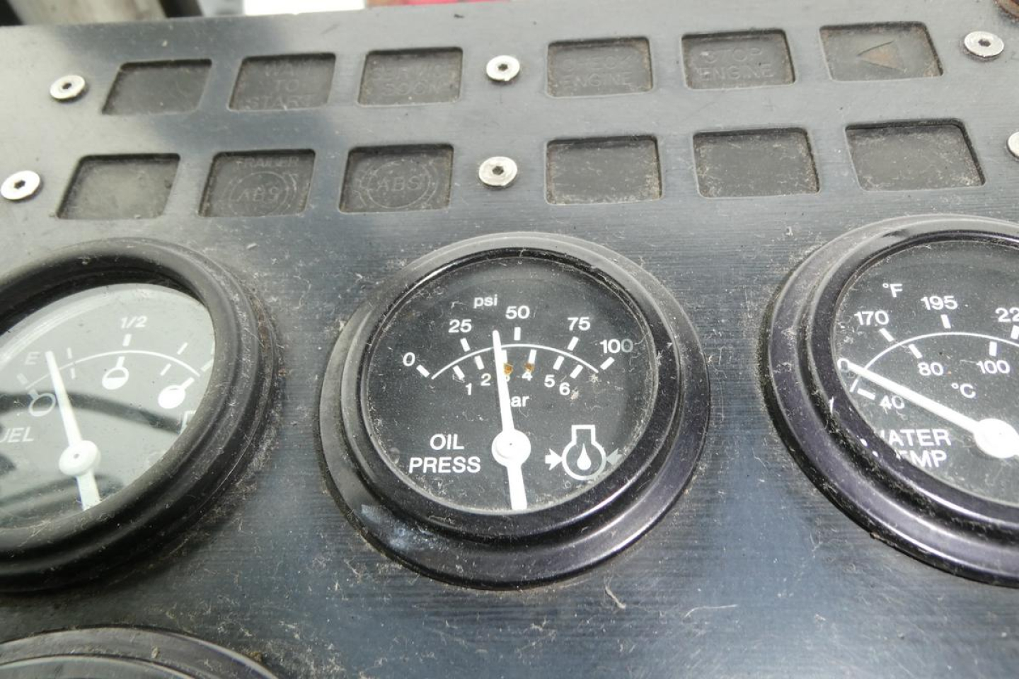 Truck dashboard gauge cluster showing oil pressure gauge and other dials in a weathered panel.