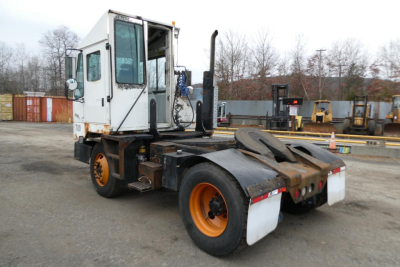 Truck yard showing a white cab and orange wheels on a yard truck chassis with wheel chocks and multiple orange and white components.