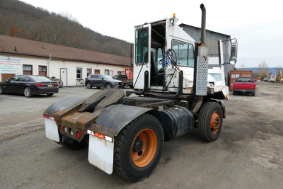 Truck chassis and cab of a used 2006 Ottawa yard truck showing rear view with dual rear axles, orange rims, fuel tanks, and exhaust stack.
