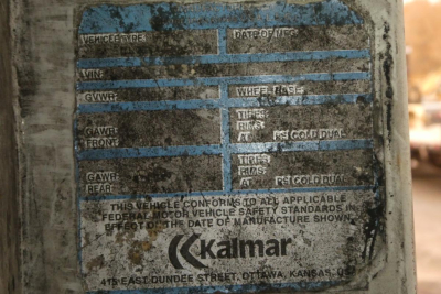 Tag plate on vehicle showing faint labels for VIN, GVWR, GAWR, wheel base, tires, and manufacturing date from Kalmar equipment.