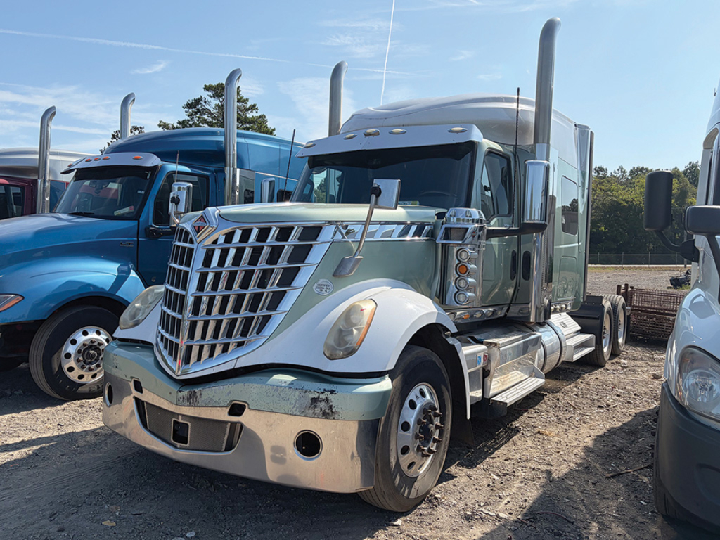 Truck cab in a dealer lot showing International LoneStar daytime running lights, chrome grille, dual exhaust stacks, and fender chrome; text on cab not legible.