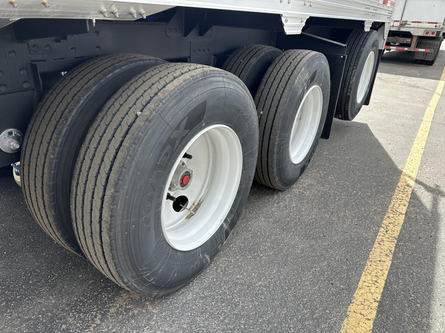Trailer wheelset close-up showing three tandem axles with white rims and black tires under a Timpte hopper trailer.