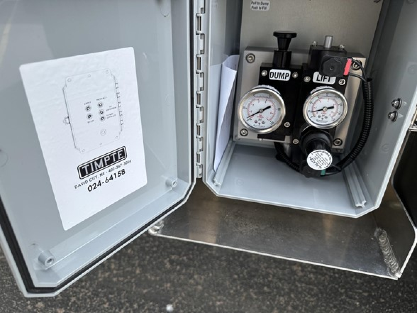 Timpte Super Hopper trailer control panel showing pump gauges labeled DUMP and LIFT inside electrical cabinet door open.
