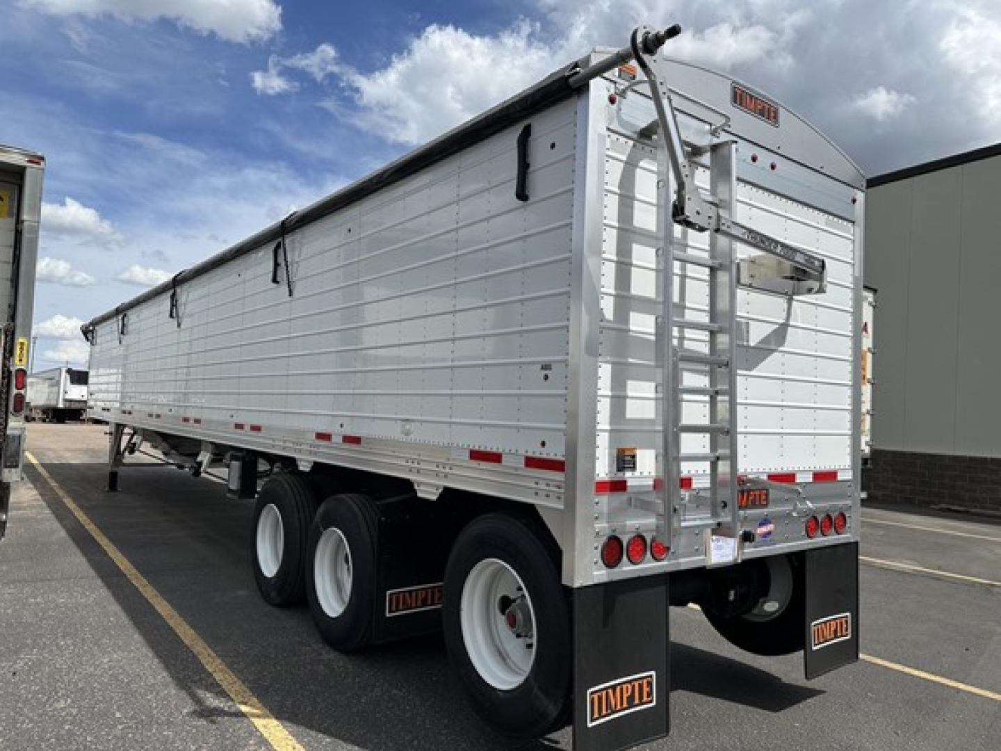 Timpte Super Hopper trailer side view showing aluminum hopper with dual rear doors and ladder, with three axles and mud flaps displaying Timpte logo.