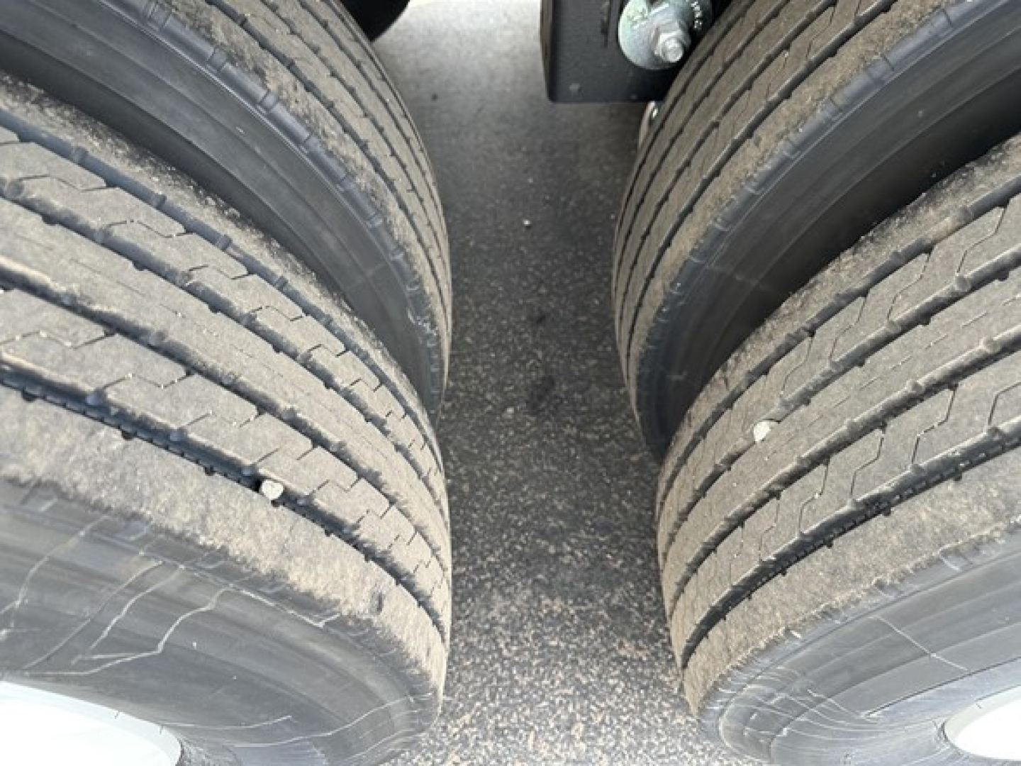 Tandem axle trailer section showing dual rear wheels and textured ground between them.