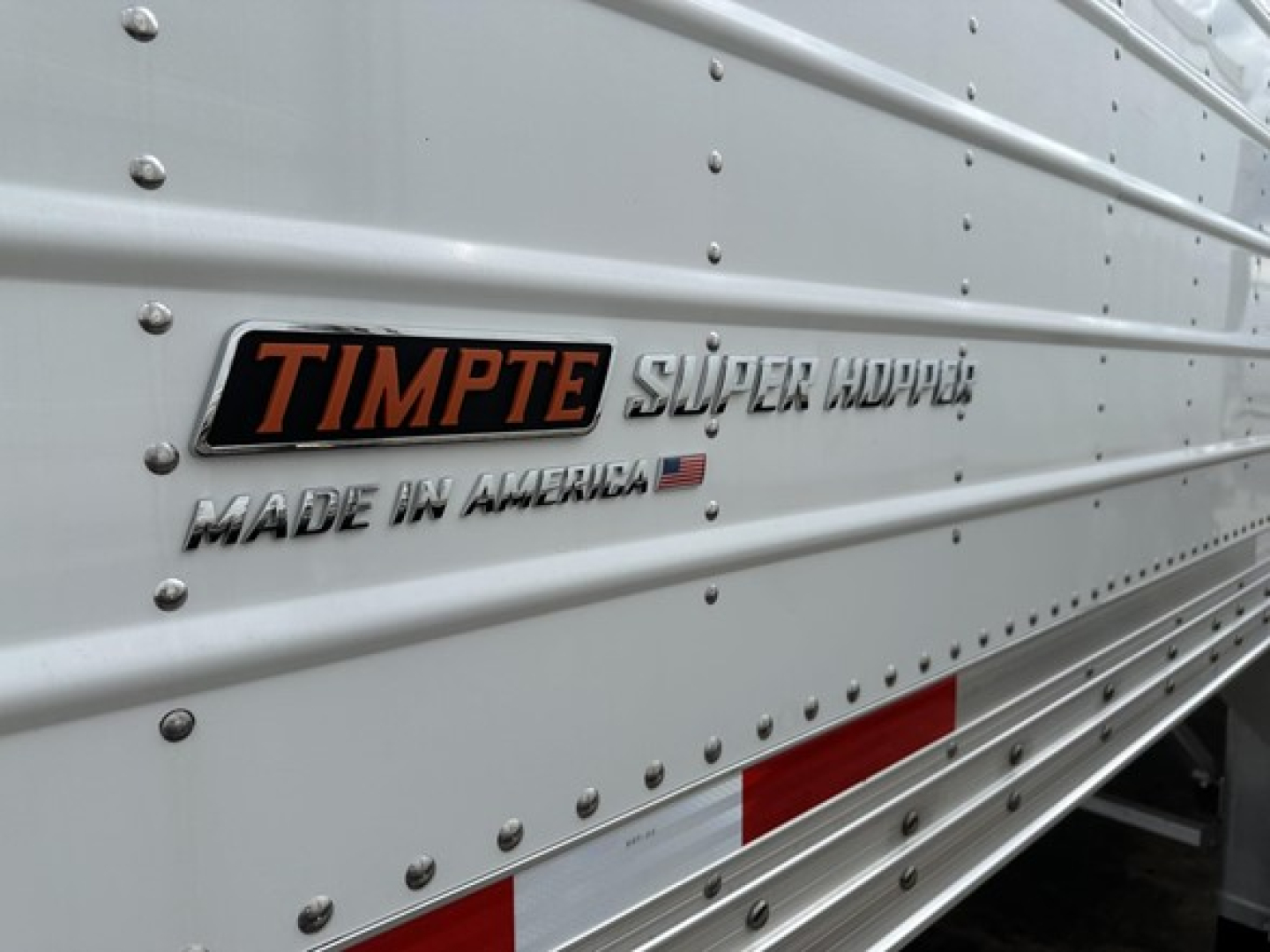 Timpte Super Hopper trailer side showing 'TIMPT E' logo, 'SUPER HOPPER' text, and 'MADE IN AMERICA' badge on riveted aluminum surface.