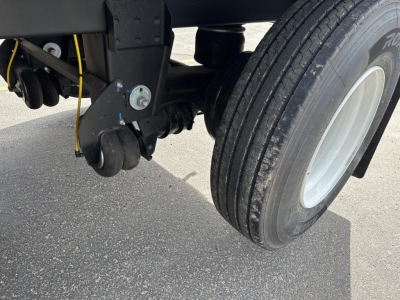 Trailer underside showing air brake chamber and leaf spring suspension near dual rear wheels; yellow cable visible.