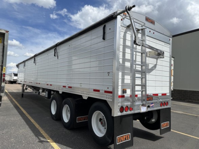 Timpte Super Hopper trailer side view showing aluminum hopper with dual rear doors and ladder, with three axles and mud flaps displaying Timpte logo.