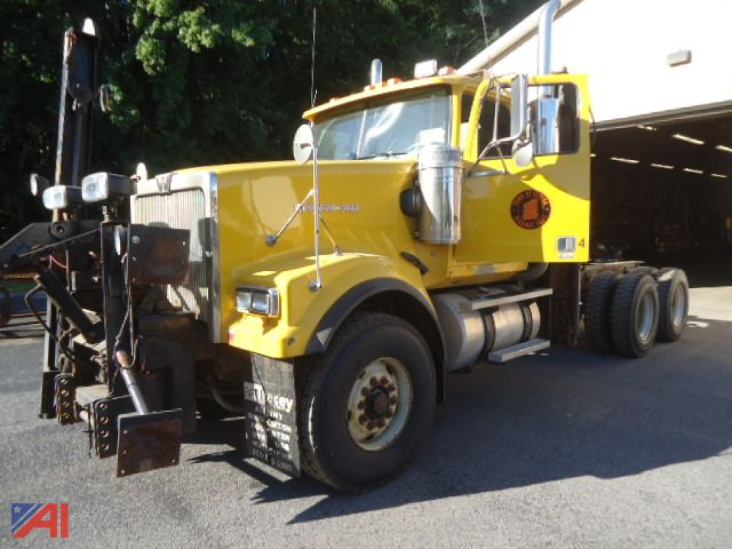 Yellow Western Star 4900 cab and chassis truck, front three-quarter view, with dual rear axles, large chrome exhaust stacks, and heavy lifting apparatus at the front.