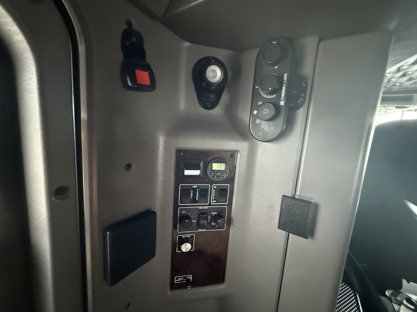 Kenworth W900L cab interior panel with switches and gauge cluster showing various controls. On panel are small digital gauge and multiple rocker switches; surrounding dash/door area.