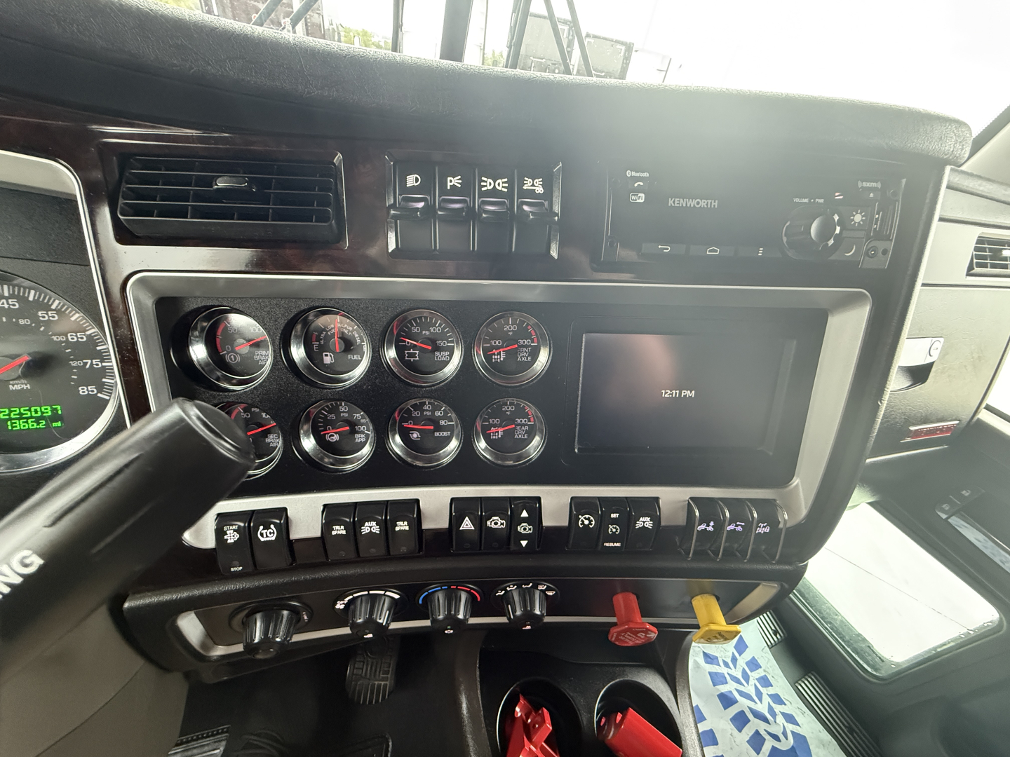 Dashboard and gauge cluster area of a Kenworth W900L truck cab, with multiple round gauges, switches, and a digital display panel visible.