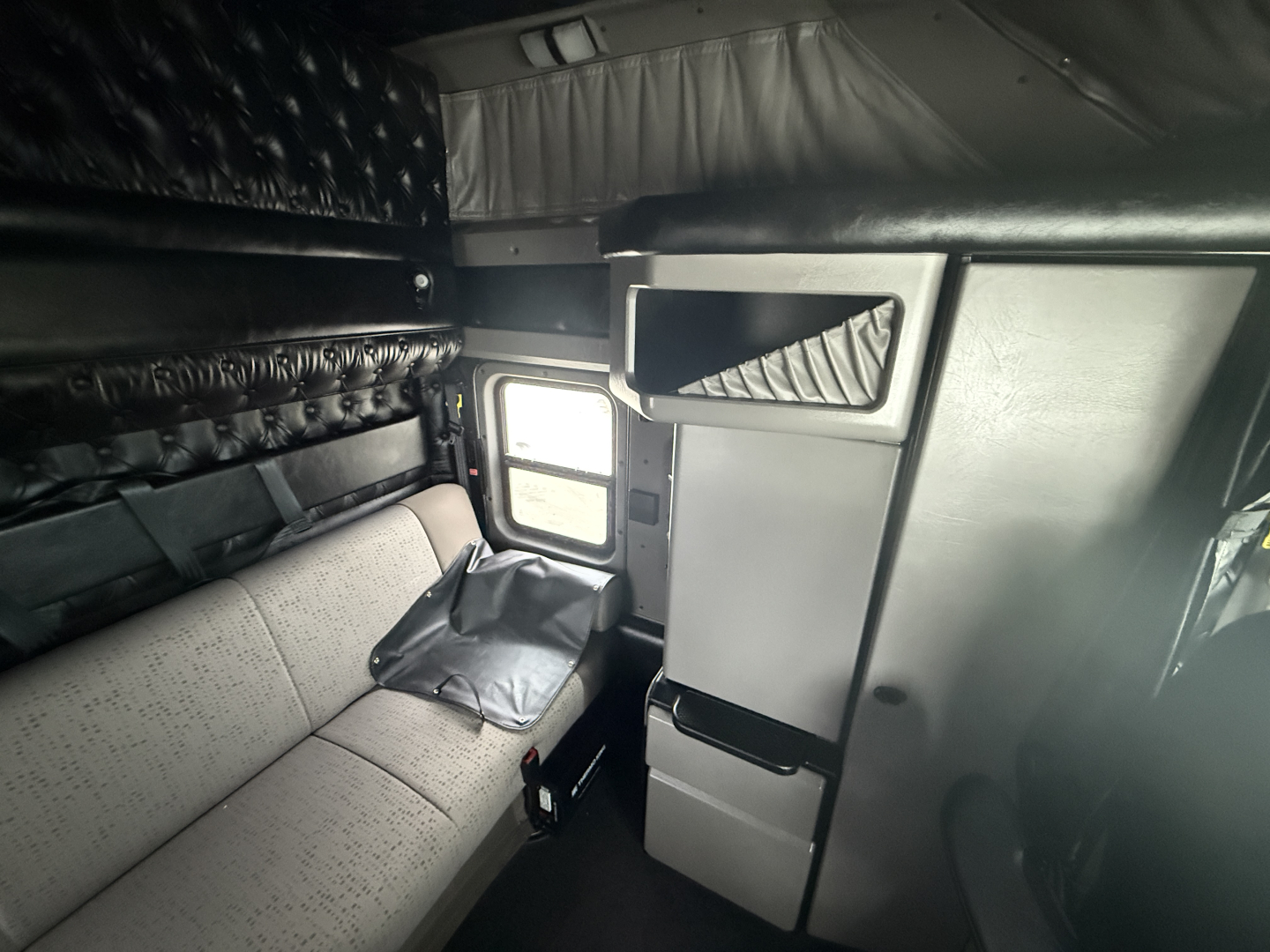 Kenworth W900L sleeper cab interior showing bunk area and storage compartments with grey upholstery.