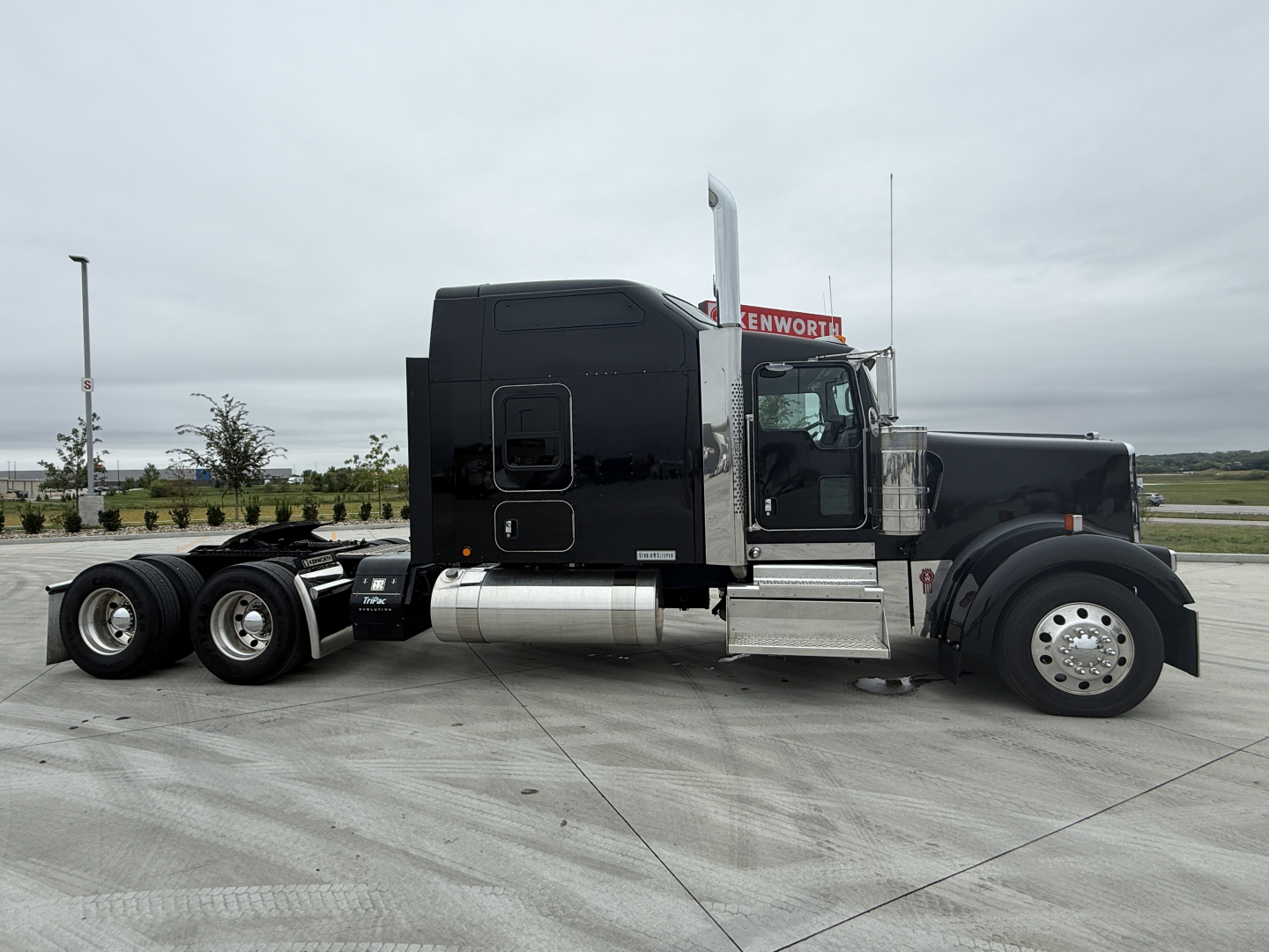 Kenworth W900L conventional sleeper truck side view showing black cab, chrome fuel tanks, aluminum steps, dual rear axles, and front wheel with alloy hubcap.