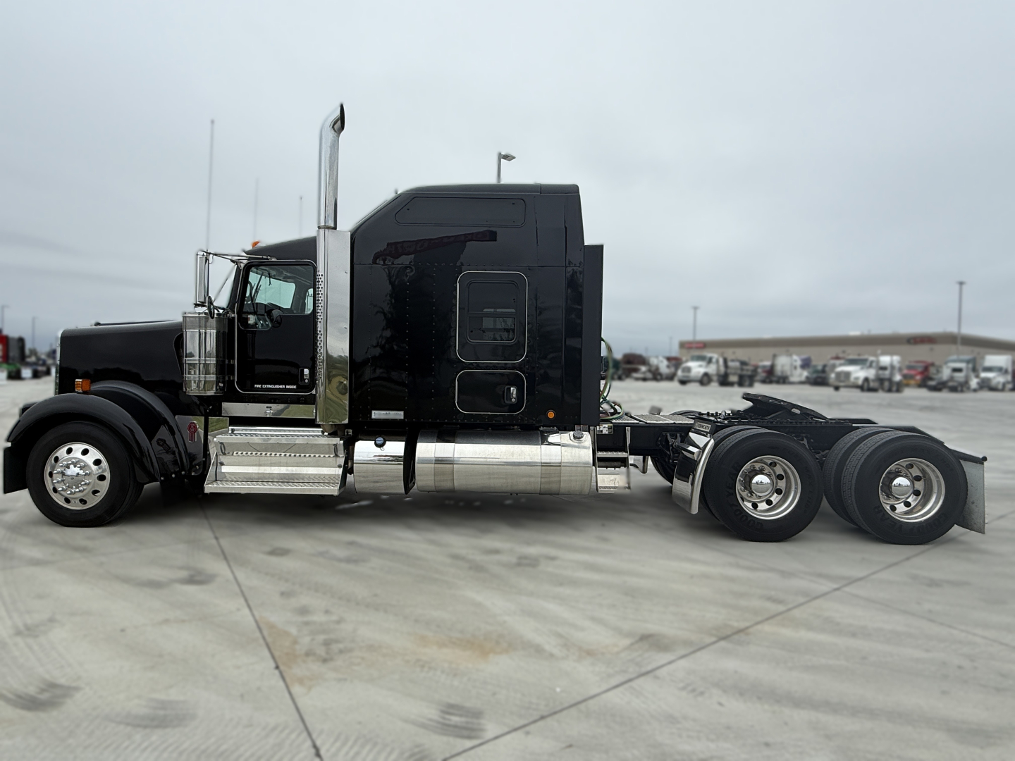 Kenworth W900L tractor in black, side view showing cab, fuel tanks, steps, and dual rear axles with wheels.