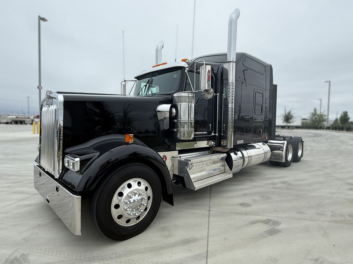 Kenworth W900L sleeper tractor truck in black with chrome exhaust stacks and polished aluminum fuel tanks; front grille and large wheels visible.