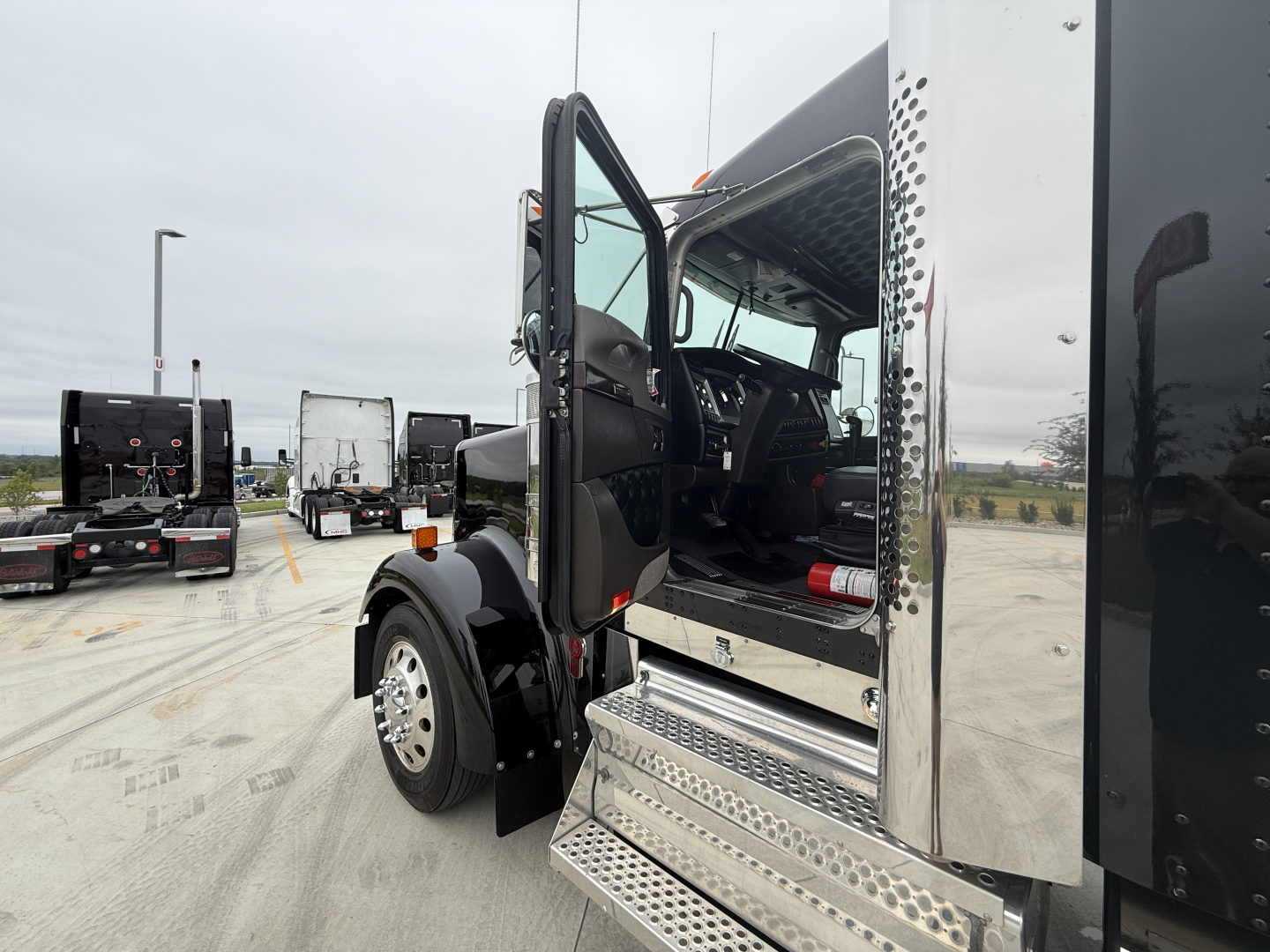 Kenworth W900L conventional sleeper cab with open door showing interior dashboard and chrome steps.