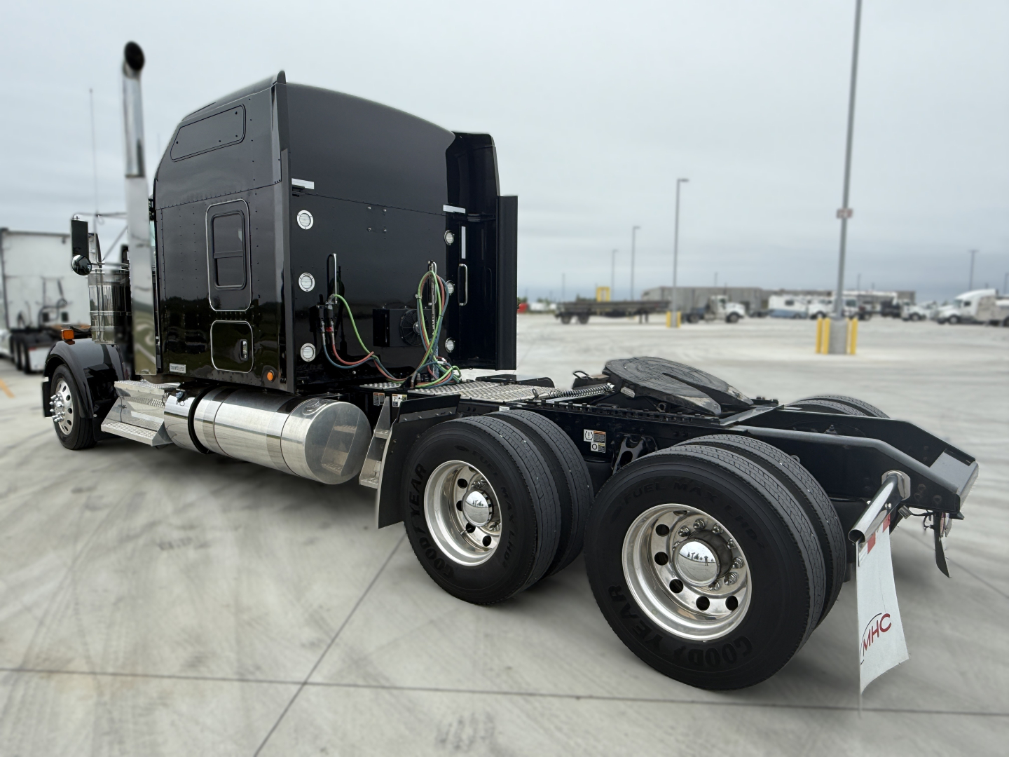 Kenworth W900L tractor chassis with black sleeper cab, rear view showing dual rear axles and fifth wheel, diesel fuel tanks, and exposed wiring.