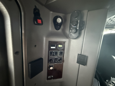 Kenworth W900L cab interior panel with switches and gauge cluster showing various controls. On panel are small digital gauge and multiple rocker switches; surrounding dash/door area.