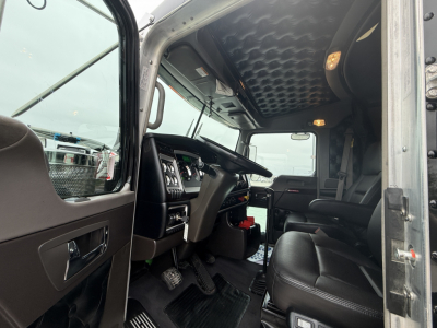 Kenworth W900L interior cab view showing steering wheel, driver's seat, dashboard, and entry door; ultra-high cabin roof with textured padding.