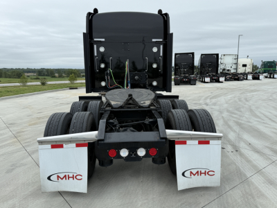 Kenworth W900L rear view showing exhausts, dual rear axles, mud flaps with MHC logos, and wiring harnesses; no visible model text other than the truck components.