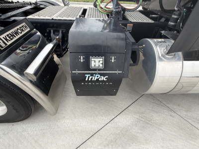 Kenworth W900L truck undercarriage showing TriPac Evolution auxiliary power unit and fuel tank with air lines and chassis components.