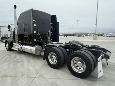 Kenworth W900L tractor chassis with black sleeper cab, rear view showing dual rear axles and fifth wheel, diesel fuel tanks, and exposed wiring.