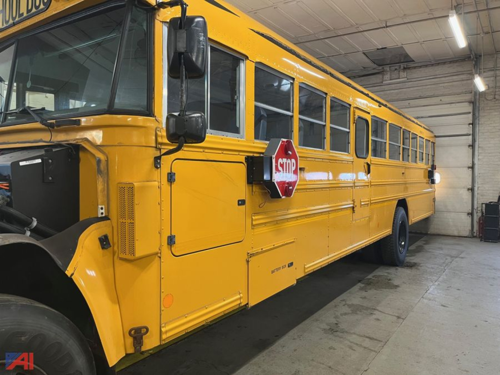 School bus side view showing yellow Blue Bird Vision bus parked indoors with door and stop sign visible.